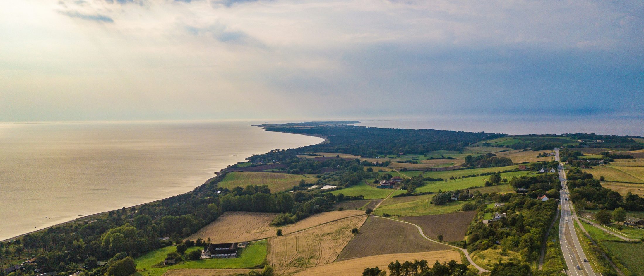 Dansk kystlandskab set fra luften med marker, skov og en landevej